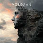 Silhouet van een menselijk gezicht gevormd uit een rotswand bij zonsondergang, met een eenzame persoon die bovenop de ‘voorhoofd’ van de rots staat en over de horizon uitkijkt; onderaan het beeld het logo ‘Voldaan’.